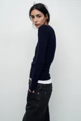 Sweater negro de punto liso con cuello redondo y mangas largas con botones dorados en los puños.