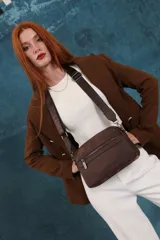 Bandolera color rosa viejo con detalles en cuero marrón claro, múltiples cremalleras metálicas y herrajes plateados. Incluye correa ancha ajustable con el logo de la marca.