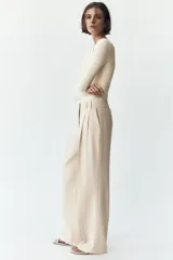 Pantalón de vestir color crema, de tiro alto y pernera ancha, con pinzas delanteras, bolsillos frontales y falsos bolsillos de doble vivo en la espalda.