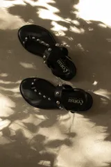 Sandalias negras de cuero sintético con tachas plateadas y ajuste con hebilla en el talón.