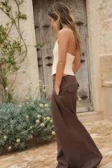 Pantalón marrón de tiro alto con trabillas, doble pliegue, bolsillos laterales y tapetas en la espalda. Pierna ancha y cierre frontal con cremallera y gancho metálico.