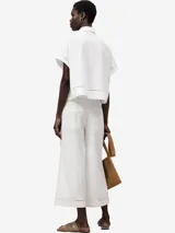 Camisa blanca de algodón con calados en el frente, ruedo y mangas. De corte recto, con cuello solapa, manga corta, botonadura frontal y bolsillo en el pecho.