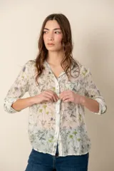 Camisa blanca con estampado floral en tonos verdes, azules y violetas, de corte clásico con cuello camisero y mangas 3/4.