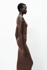 Vestido midi negro de punto, con cuello asimétrico, manga sisa, aplique metálico dorado en el hombro y drapeado lateral.