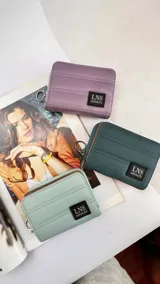 Billetera corta con cierre alrededor y tapa, confeccionada en tela capitoneada. Incluye varias reparticiones con tarjeteros y bolsillos internos, y una correa de mano desmontable. Disponible en negro, rojo y dorado.