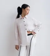 Camisa de lino color blanco, de corte recto y mangas largas, con botones negros y aberturas laterales.