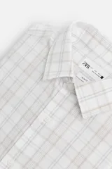 Camisa de vestir slim fit de algodón, color blanco con diseño de cuadros en tonos grises y beige. Tiene cuello italiano, mangas largas con puños abotonados y cierre frontal con botones.