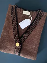 Chaleco marrón de punto con escote en V, bordado con botones dorados. Tejido a mano con algodón y detalles de lurex. Terminaciones en crochet y bordados hechos a mano con lana merino.
