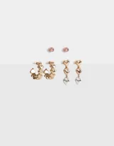 Set de tres pares de aros pasantes: un par de strass rosa, un par de argollas doradas con corazones y un par de aros colgantes con corazones dorados y plateados.