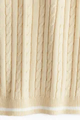 Top color crema en tejido de punto trenzado, con cuello redondo y mangas cortas con ribete blanco.