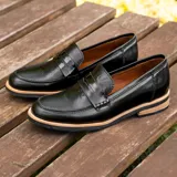 Mocasín de cuero vacuno color marrón, con detalle de antifaz en gamuza. Tiene taco de madera foliado en cuero de 2,5cm y entre suela de goma de 1cm.