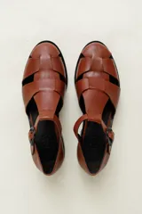Sandalia roja de cuero vacuno con diseño de tiras entrecruzadas y hebilla lateral. Tiene suela de cuero artesanal y taco bajo.
