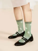 Medias de caña media color verde menta traslúcido con puño marrón con volados y estampado de tréboles blancos.