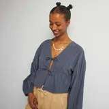 Blusa azul de algodón con textura arrugada, escote en V con lazos y mangas largas abullonadas.