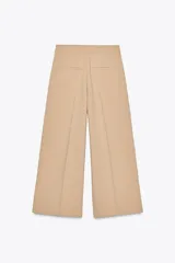Pantalón culotte color beige de tiro alto con bolsillos delanteros y falsos bolsillos de vivo en la espalda. Pierna ancha y corta. Cierre frontal con cremallera, botón interior y gancho.