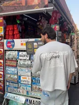 Remera rosa de corte recto con estampado en la espalda que incluye el texto "Itta Tours", "Tour", y nombres de ciudades como Ibiza, Madrid, Andorra, Barcelona y Formentera.