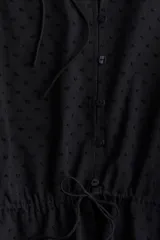 Blusa negra de algodón con textura de lunares, escote redondo con lazo, mangas tres cuartos abullonadas, botones frontales y cintura ajustable con cordón.