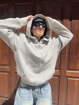 Campera con capucha y cierre frontal, color hueso con rayas finas horizontales en tono oscuro. Presenta un calce holgado (boxy fit) y puños y cintura acanalados.