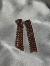 Par de aros colgantes con base rectangular y flecos de strass color cobre. Cierre con tuerca a presión.