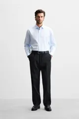 Camisa celeste a rayas verticales, de corte regular, confeccionada en algodón, con cuello italiano, manga larga con puños abotonados y cierre frontal con botones.