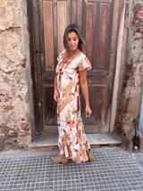 Vestido largo con estampado abstracto en tonos camel, naranja y blanco, con escote en V, mangas cortas con volados y falda con volados en el ruedo.