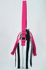 Bolso tipo tote bag con diseño a rayas verticales blancas y negras, doble asa de mano rosa y correa de hombro ajustable y removible también rosa.
