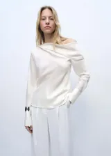 Blusa color blanco hueso de tejido satinado, con cuello drapeado y mangas largas con puños abiertos.