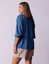 Blusa celeste de tencel con cuello a la base, escote en V con aplique de cordel y lazo de ajuste. Manga larga amplia con puño elastizado.