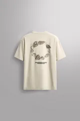 Camiseta color crema de corte holgado, cuello redondo y manga corta. Presenta un pequeño estampado con texto en el lado izquierdo del pecho.