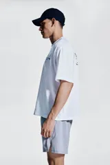 Remera deportiva blanca de corte boxy, confeccionada en tejido funcional DryMove™ que ayuda a absorber el sudor. Tiene cuello redondo ribeteado y hombros levemente caídos. Estampado en el frente con flechas y el número 012 en color celeste.