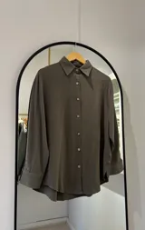 Camisa clásica verde oliva, de manga larga con cuello camisero. Cierre frontal con botones de coco y laterales con abertura.