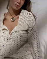 Collar con dije dorado irregular con agujero central, colgando de cordón negro ajustable.