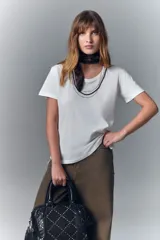 Remera blanca de algodón con cuello redondo y aplique de cadenas metálicas y strass en el escote.
