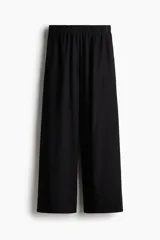 Pantalón negro de corte holgado, tiro alto con cintura elástica y piernas amplias. Confeccionado en tejido liviano de lino y viscosa. Presenta bolsillos al bies y bolsillos decorativos insertados atrás.