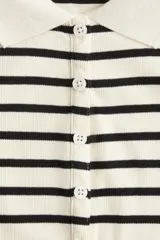 Remera polo entallada en punto acanalado a rayas horizontales negras y crudas, con cuello clásico y tapeta de botones.