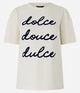 Remera color crema de algodón con cuello redondo y mangas cortas abullonadas. Estampa frontal con la frase "dolce douce dulce" en letras cursivas azul marino.