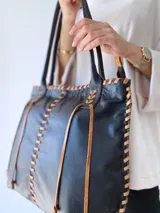 Bolso tipo tote de cuero negro con costuras a la vista en color camel. Tiene doble asa de hombro y está forrada en tela.