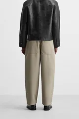 Pantalón negro de corte amplio tipo balloon fit, con cintura con pliegues frontales, bolsillos delanteros y traseros de plastrón. Cierre frontal con cremallera y botón.