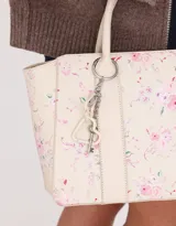 Cartera tipo tote color blanco crudo, con doble asa corta y correa larga regulable y desmontable. Incluye charm colgante con forma de corazón y cierre superior.