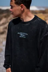 Buzo negro de corte holgado con cuello redondo y mangas largas. Estampado frontal con el texto "Glassy Waves Beach Life".
