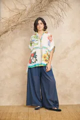 Camisa de manga corta con cuello clásico y cierre frontal con botones. Presenta un estampado con motivos florales, frutales y paisajes.