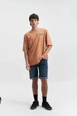 Remera de manga corta color salmón, de corte holgado con estampado en la espalda que incluye una flor con cara y texto.