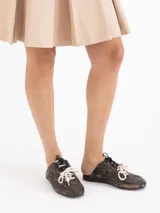 Zapatilla tipo mule (sin talón) de cuero vacuno, color celeste con efecto gastado y detalles de recortes. Presenta un logo estilizado en el lateral y cordones anchos de color beige y marrón.