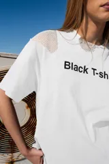 Remera blanca de algodón con corte relajado, mangas cortas y detalles de malla en los hombros. Estampado frontal con la frase "Black T-shirt" en letras negras.