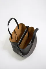 Bolso tote negro de cuero vacuno con doble asa corta y correa de tela extraíble. Interior con tres compartimentos y bolsillo con cremallera. Logo metálico de la marca en el frente.