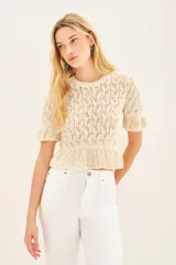 Sweater color crema tejido con punto desagujado en hilado de algodón y poliéster. Tiene ajustes en mangas y cintura, y pequeños volados en las terminaciones.