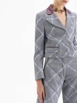 Chaqueta corta (cropped) con estampado a cuadros gris y azul claro, cuello solapa de cuero color bordó y bordados a juego. Presenta bolsillos con tapa en el frente y mangas con puños acampanados.