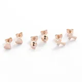 Set de tres pares de aros mini color oro rosa en acero quirúrgico: un par con forma de cubo con cristal, un par con forma circular y un par con forma de barra horizontal.