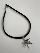 Gargantilla negra de tiento de cuero natural con dije de acero quirúrgico hipoalergénico en forma de flor.
