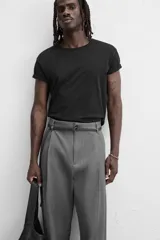 Pantalón gris de corte ancho con pliegues frontales y cinturón fino negro.